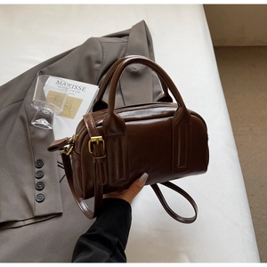 Détail du sac Boston en cuir brillant marron foncé avec finitions dorées et bandoulière