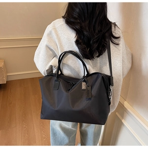 Detail of a large black nylon travel tote featuring a side leather tag and wide shoulder strap