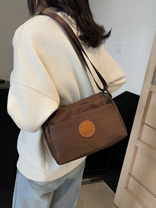 Sac à bandoulière carré marron foncé en nylon porté par un mannequin en sweat blanc