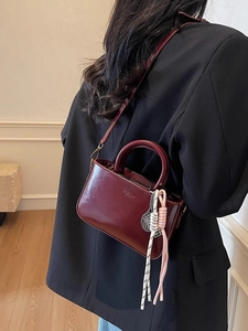 Vintage burgundy leather handbag with round handles and detachable strap on black blazer