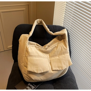 Quilted beige tote bag with two front pockets placed on a black corduroy chair