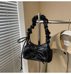 Detail of a black patent leather shoulder bag with a bow and ruched handle