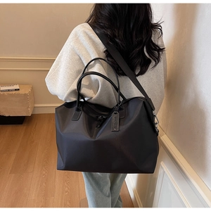 Detailed shot of a black nylon tote bag showing double handles and leather charm decoration