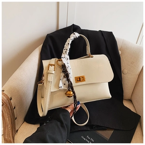 Detail of cream white handbag with silk scarf handle and golden lock on an armchair