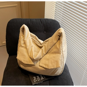Detailed close-up of a large beige quilted tote bag on a black corduroy chair indoors