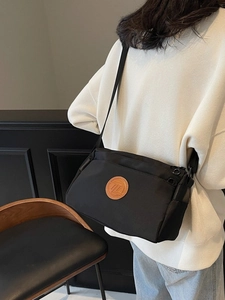 Sac à bandoulière carré noir minimaliste avec un patch logo rond en cuir marron