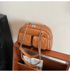 Detail of tan quilted pillow bag showing double zippers and silver chain on wood rack