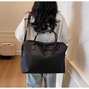 Rear view of a model carrying a large black nylon tote bag with leather tag detail