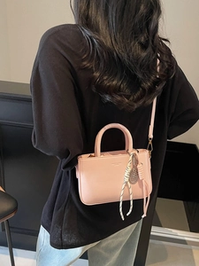 Pink minimalist crossbody bag with tennis racket charm worn over a casual black outfit