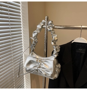 Detail of silver metallic handbag featuring ruched bow design and ruffled handle strap