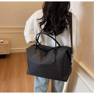 Rear view of a model carrying a large black nylon travel tote bag in a minimalist room
