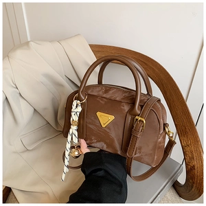 Détail d'un sac bowling en cuir marron avec logo triangulaire doré sur une chaise