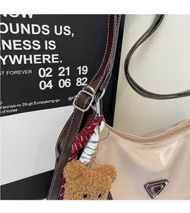 Detail einer cremeweißen Beuteltasche aus Kunstleder mit Dreieckslogo und braunem Bärenanhänger