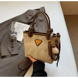 Detail of khaki canvas tote bag featuring brown leather trim and plush ice cream charm