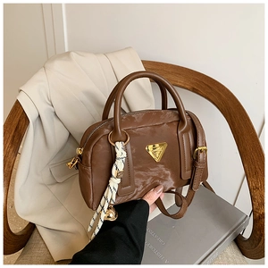 Sac Boston en similicuir marron avec plaque triangle dorée et foulard rayé sur une chaise