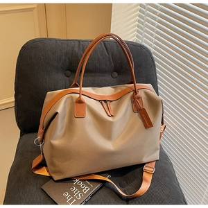 Detail of khaki nylon tote bag with leather handles and metallic zippers on a chair