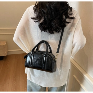 Sac Boston chic en cuir verni noir avec double poignée et une fine bandoulière amovible