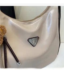 Detail der cremefarbenen Lackleder-Tote Bag mit Glanzeffekt und Metall-Dreiecksplakette