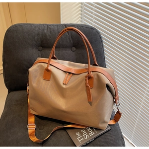 Detail of khaki nylon travel tote bag with brown leather handles on a grey corduroy chair