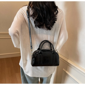 Détail d'un sac Boston en cuir noir brillant porté en bandoulière pour un style chic
