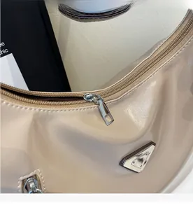 Detail eines glatten Silberreißverschlusses und Dreiecksplakette an einer beigen Hobo-Tasche