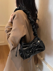 Chic black patent leather shoulder bag with pleated strap and bow detail on a model