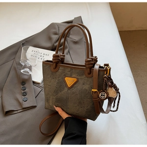Detail of gray-green fabric tote bag with brown leather trim and knotted charm