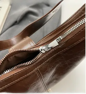 Close-up of smooth metal zipper on a brown vintage-style oily leather hobo bag for women