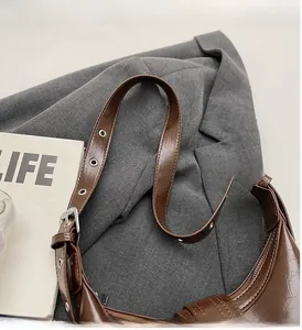 Detail of a brown leather shoulder bag with adjustable strap on a gray blazer context