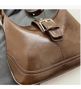 Detail of dark brown crinkled leather shoulder bag with white stitching and metal buckle