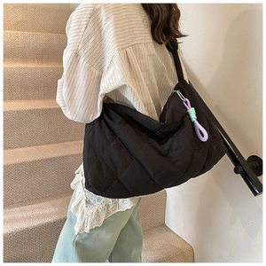 Close-up of black quilted tote bag with colorful zipper pull shown on model's shoulder