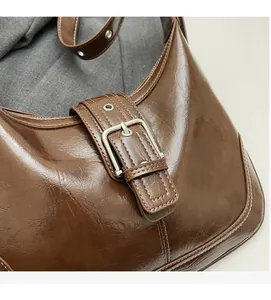Detailed view of brown glossy leather hobo bag featuring silver buckle and stitching