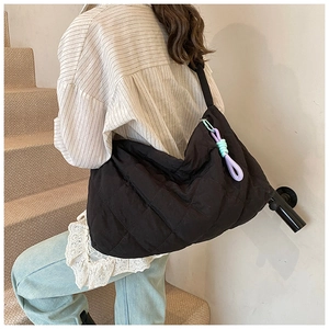 Detail of black quilted tote bag with colorful braided knot charm and wide shoulder strap