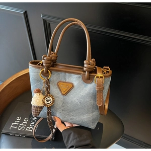 Close-up of blue denim bucket bag with brown leather handles and knotted strap detail