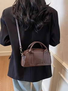 Sac Boston vintage marron brillant avec deux poignées et bandoulière porté par un mannequin