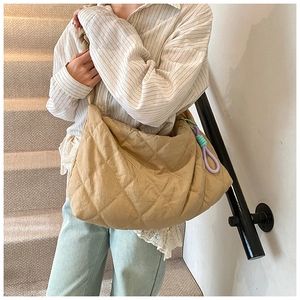 Quilted khaki tote bag featuring knotted charm pendant shown on model in modern setting