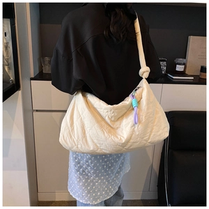 Detail of beige quilted tote bag featuring a knotted shoulder strap and colorful zipper cords