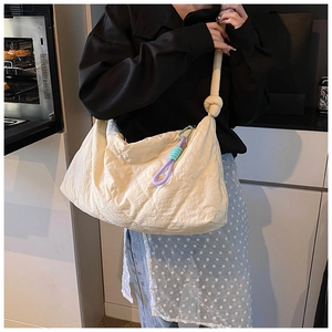 Detail of cream quilted tote bag with knot strap and colorful woven charm on shoulder