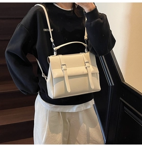 Dettaglio di una borsa in pelle bianco crema con patta e fibbie metalliche decorative