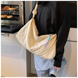Close-up of beige quilted hobo bag featuring a knotted strap and colorful braided zipper pulls