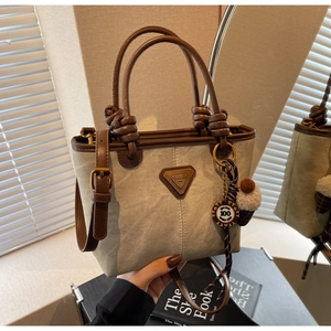 Detail of canvas bucket bag featuring dark brown leather trim and knotted handle accents