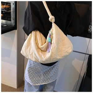 Large quilted cream shoulder bag showing the knotted strap and woven charm detail