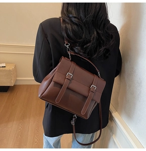 Dettaglio borsa a tracolla in pelle marrone scuro con fibbie in metallo su un blazer nero