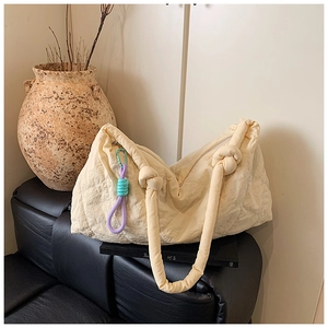 Detailed view of cream quilted tote bag featuring a knotted handle and woven charm accessory