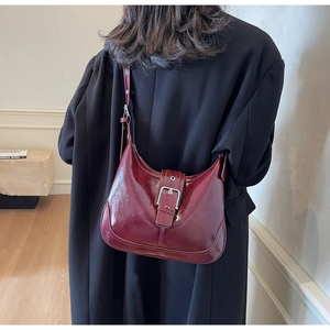 Detailansicht der burgunderroten Lackleder-Schultertasche mit Silberschnalle an einem Modell