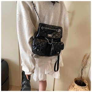 Detail view of black quilted backpack with silver chains and flap pockets worn on person