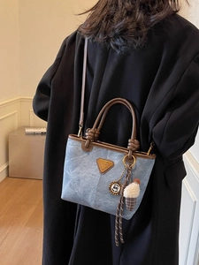 Blue denim crossbody bucket bag with brown leather handles and decorative charms on a model