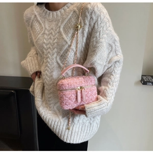 Pink tweed box bag with golden chain strap worn by a model in a minimalist setting