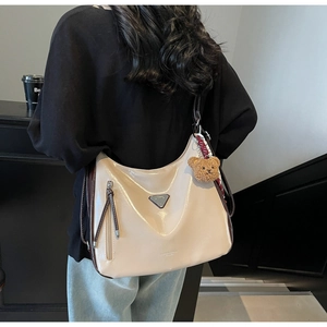 Detail der cremefarbenen Hobo-Tasche mit dunkelbraunem Riemen und Plüschbär-Anhänger