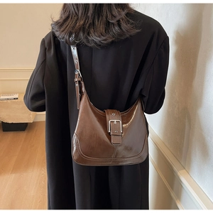 Detailansicht braune glänzende PU-Schultertasche mit Silberschnalle auf schwarzem Mantel